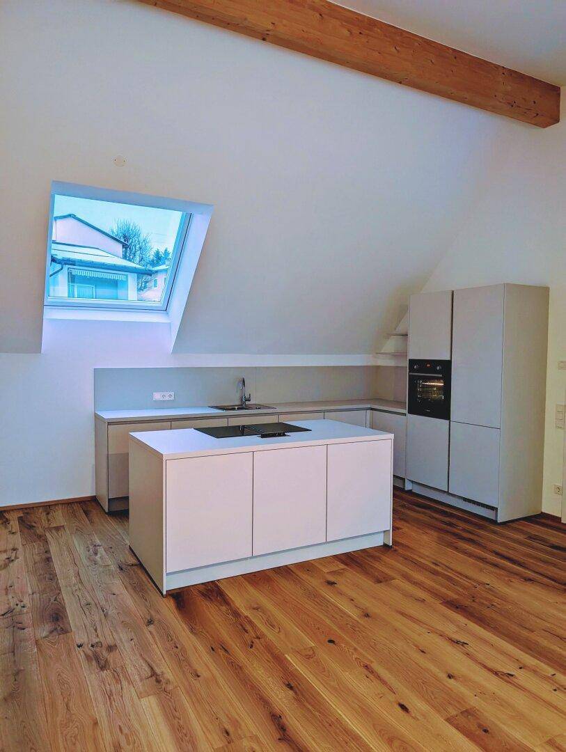 Moderne Küche im Dachgeschoss mit Schrägdach, Dachfenster, Kochinsel und sichtbarem Holzbalken.
