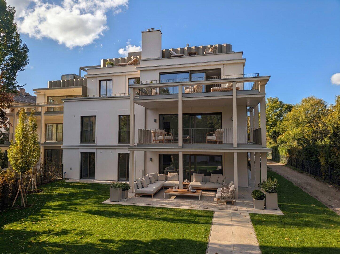 Moderne Wohnanlage mit weißer Fassade, großzügigen Balkonen, einer Terrasse und gepflegtem Rasen.