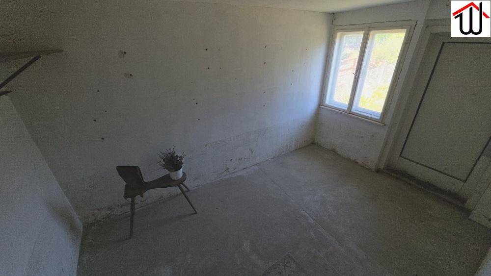 Leerer Raum mit Betonboden, weißen Wänden und einem Fenster, bereit für die Renovierung.