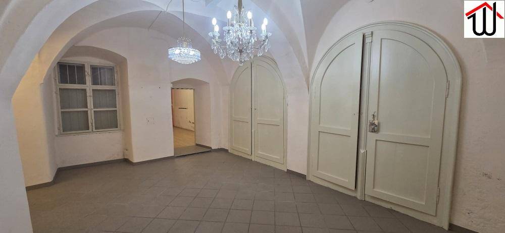 Großer Raum mit beeindruckenden Gewölbedecken, grauen Fliesen, einem Fenster und zwei eleganten Flügeltüren.