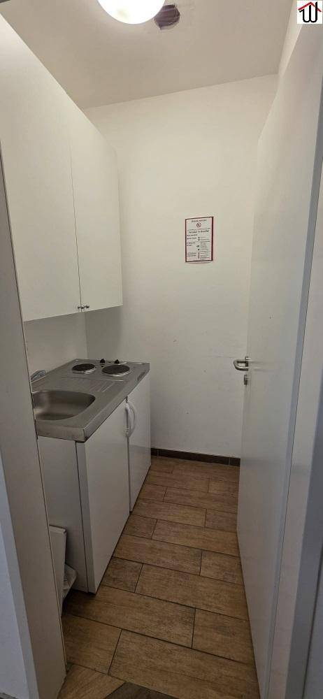 Kleine Küchenzeile mit weißen Schränken, Spüle und zwei Kochplatten auf Holzboden.
