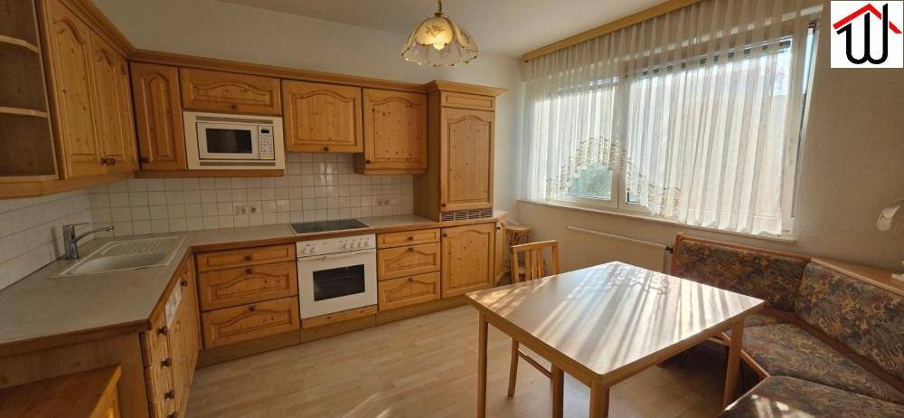 Helle Wohnküche mit Holzschränken, Einbaugeräten und Esstisch, ideal für gemeinsame Mahlzeiten.