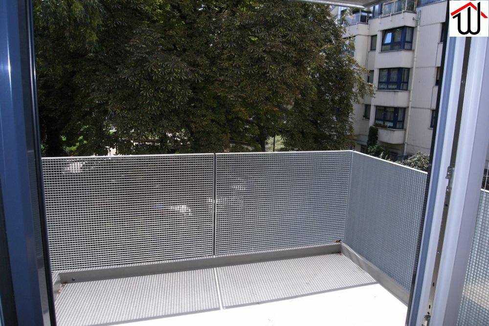 Balkon mit Metallgeländer und Blick auf Bäume und umliegende Gebäude.