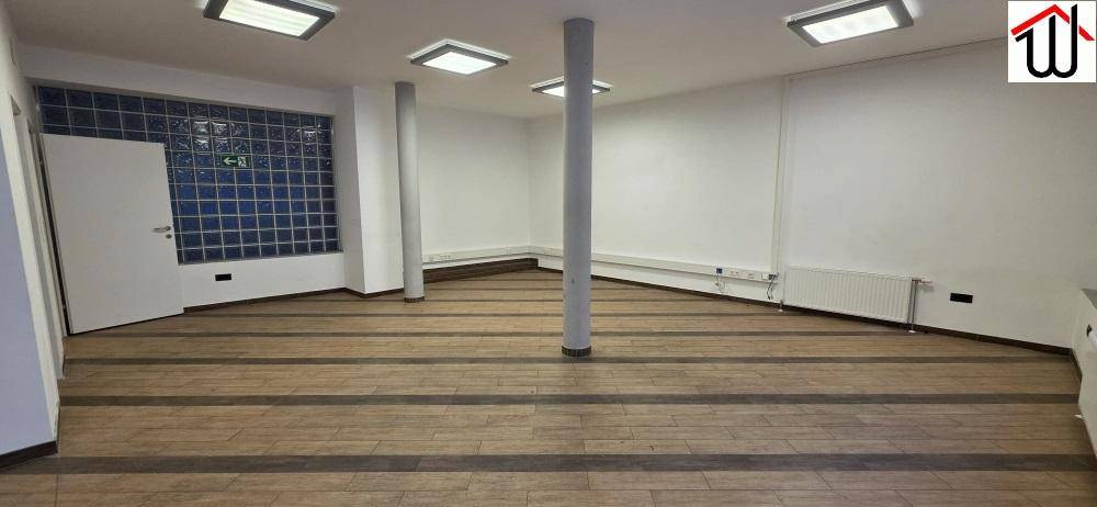 Geräumiger Büroraum mit Glasbausteinwand, weißer Tür und Holzboden in gutem Zustand.