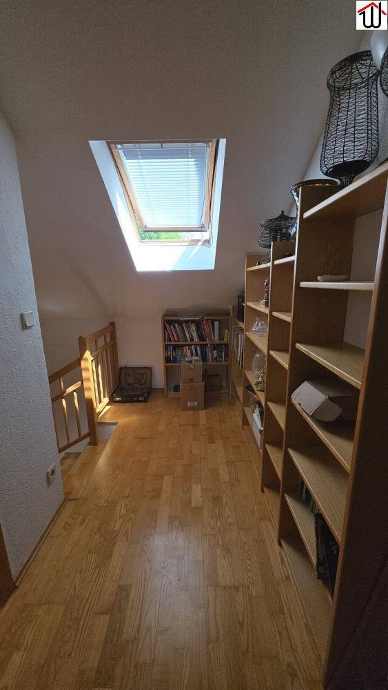 Dachgeschossflur mit Holzboden, Bücherregalen und einem Dachfenster für Tageslicht.
