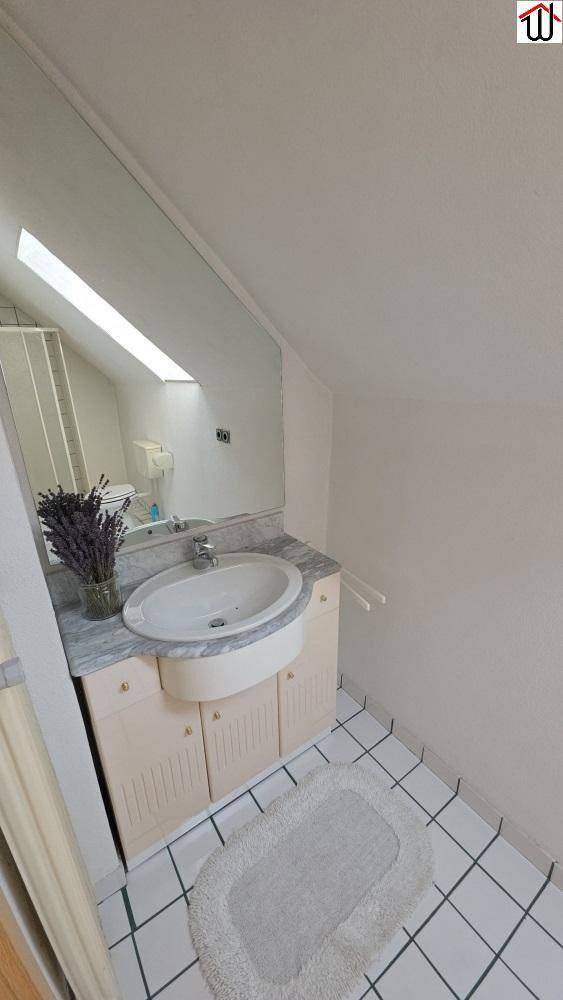 Modernes Badezimmer mit Einzelwaschbecken, großem Spiegel, weißen Fliesen und Dachschräge mit Oberlicht.