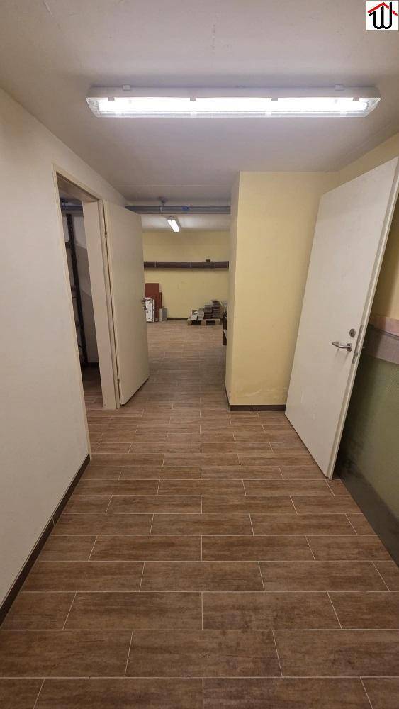 Heller Flur mit holzgemusterten Fliesen, weißen Türen und Deckenbeleuchtung, der zu weiteren Räumen führt.