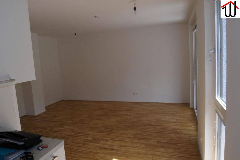Geräumiges Wohnzimmer mit Holzboden, weißen Wänden und viel Tageslicht.