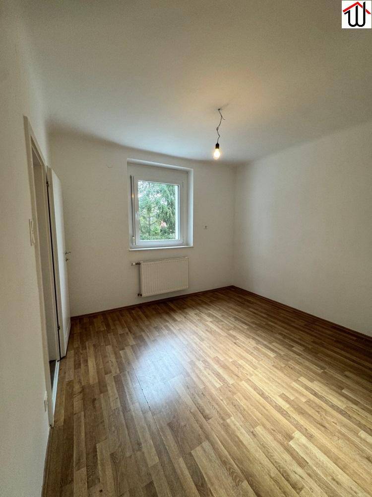 Ruhiges Schlafzimmer mit Laminatboden und einem Fenster, das viel Tageslicht hereinlässt.