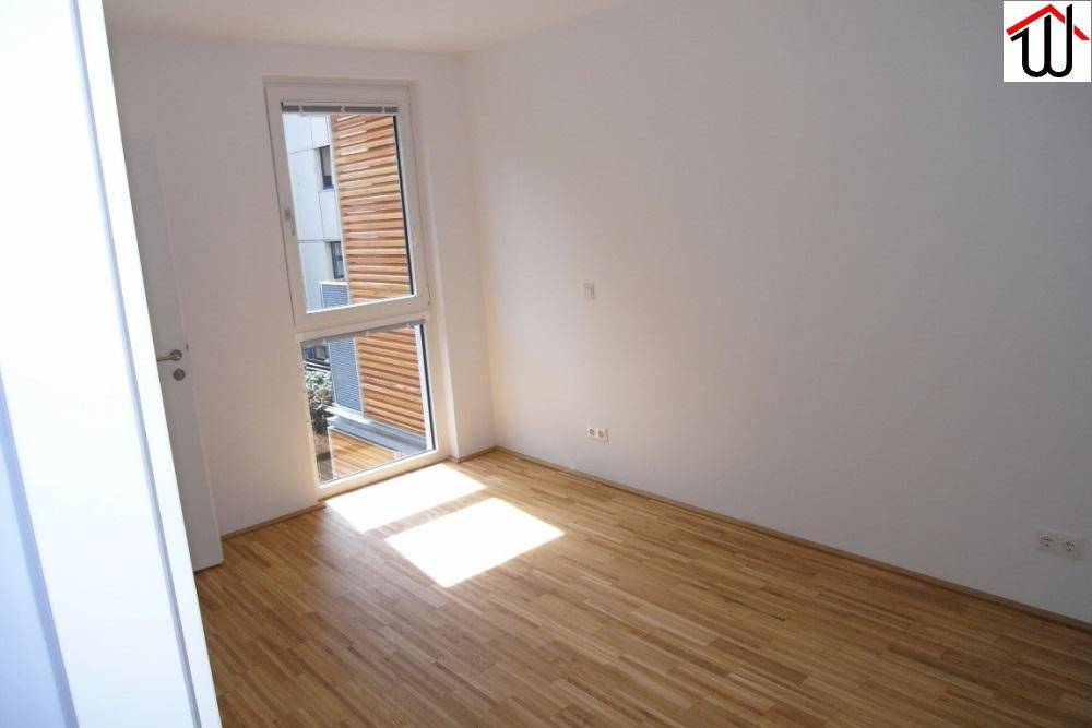 Schlafzimmer mit hellem Holzboden, weißen Wänden und einem großen Fenster.