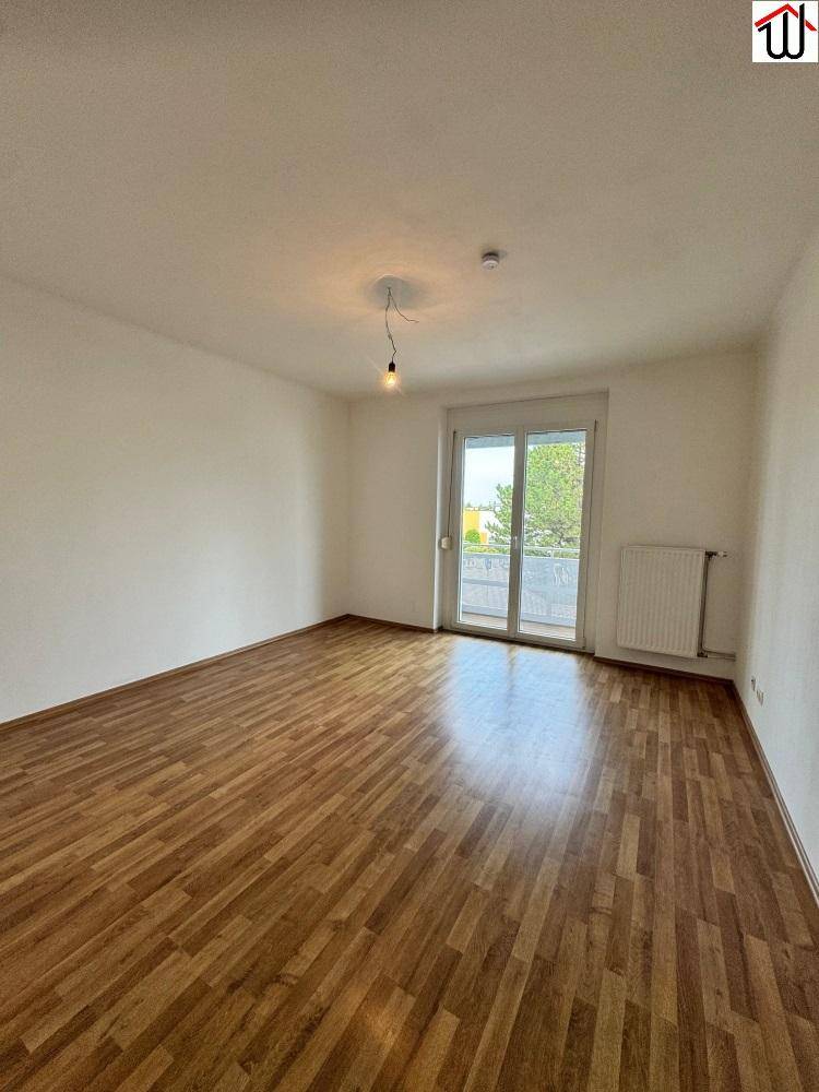Heller Wohnraum mit Laminatboden und Zugang zu einem Balkon, ideal für entspannte Stunden.