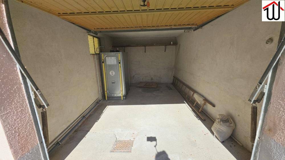 Geräumige Garage mit Betonboden, Holzdecke und Rolltor, bietet Platz für ein Fahrzeug.