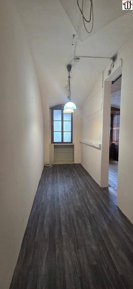 Langer, schmaler Flur mit dunklem Laminatboden und einem Fenster am Ende, das Tageslicht hereinlässt.