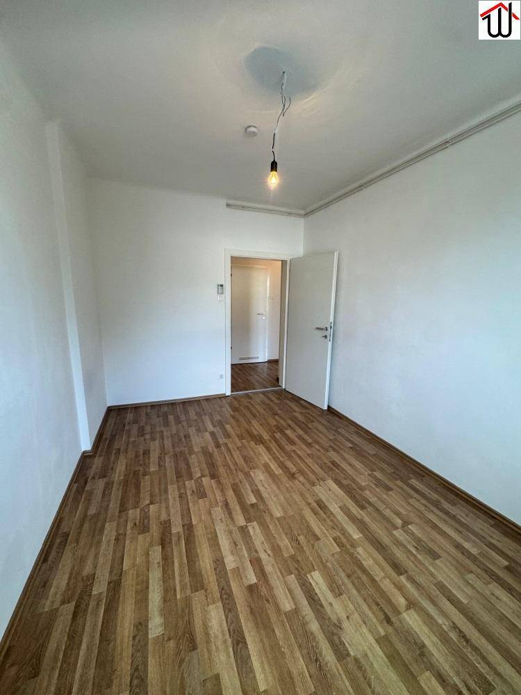 Leerer Raum mit Laminatboden und weiß gestrichenen Wänden, bereit zur individuellen Gestaltung.