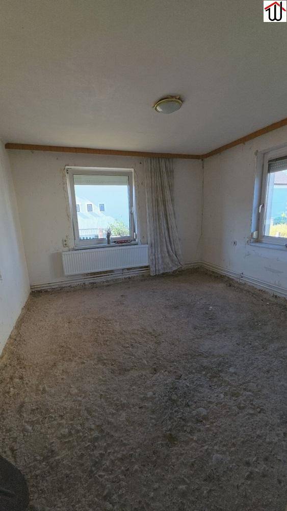Heller, leerer Raum in Renovierung mit unfertigem Boden und zwei Fenstern für viel Tageslicht.