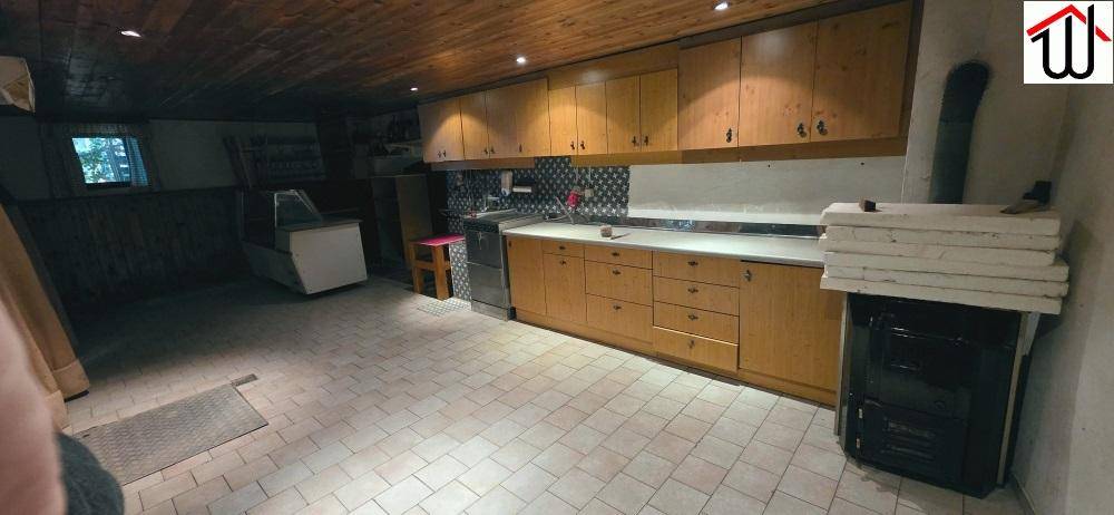 Rustikale Küche mit Holzschränken, Fliesenboden und einem traditionellen Holzofen.