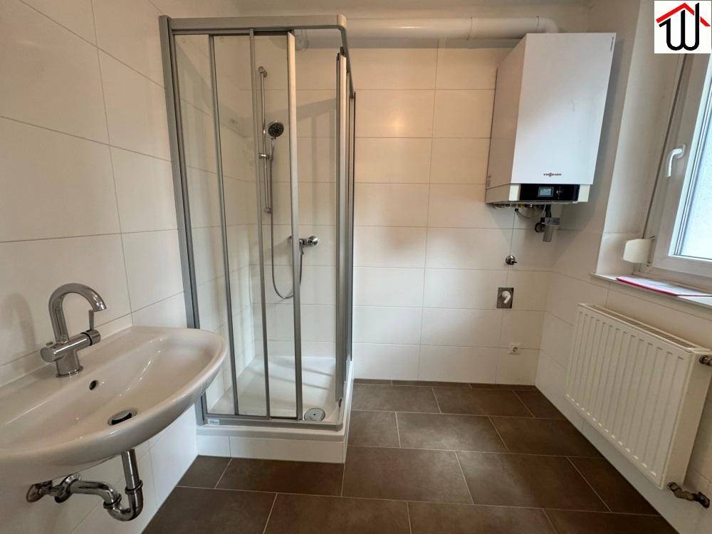 Modernes Badezimmer mit Duschkabine, Waschbecken und Gastherme, hell gefliest.