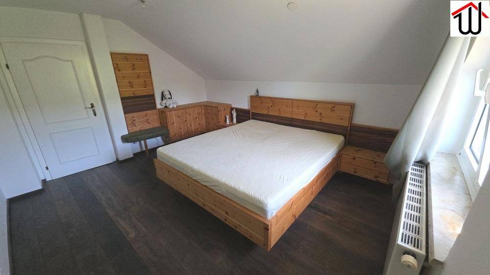 Gemütliches Schlafzimmer mit Holzbett, Holzboden und schrägen Wänden im Dachgeschoss.