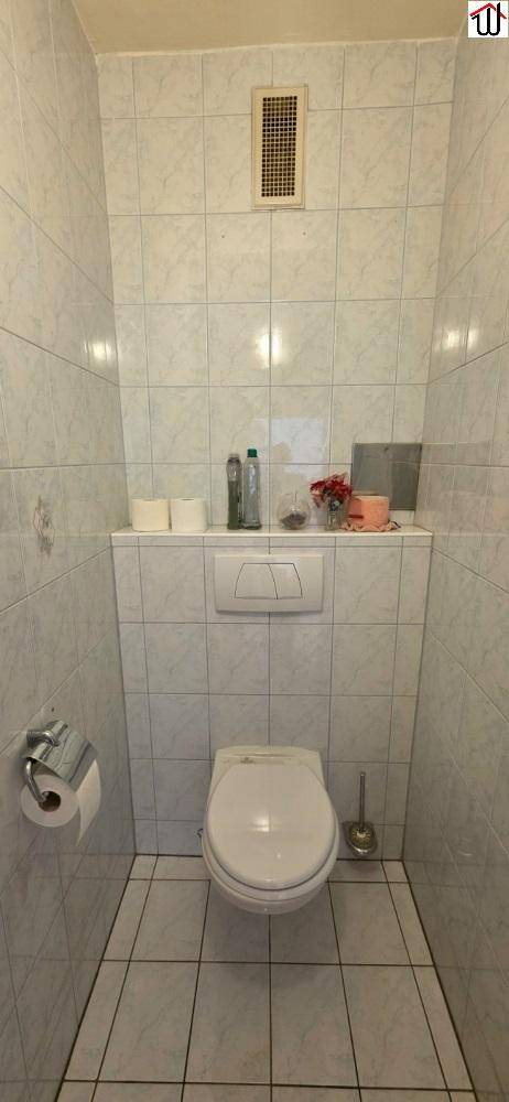 Separates WC mit Wand-WC und hellen Fliesen an Wänden und Boden, einfach und funktional gestaltet.