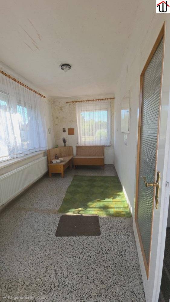 Heller, verglaster Vorraum mit Fenstern, grünem Teppich und einfacher Einrichtung, renovierungsbedürftig.