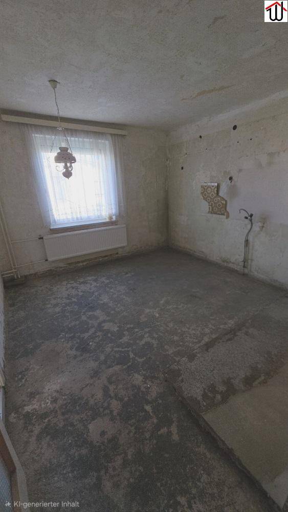 Renovierungsbedürftiger Raum mit unfertigem Boden, beschädigten Wänden und einem Fenster mit Vorhang.