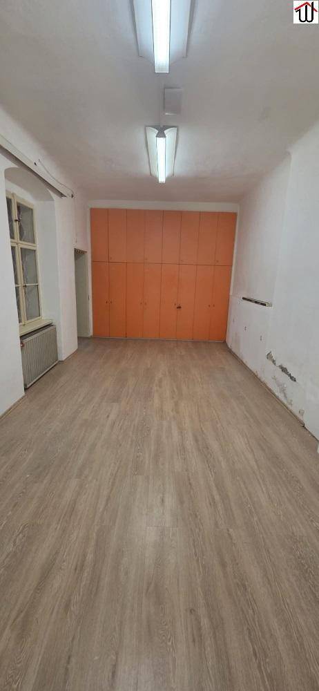 Heller Raum mit Holzoptik-Boden, einer Wand aus orangefarbenen Einbauschränken und einem Fenster.