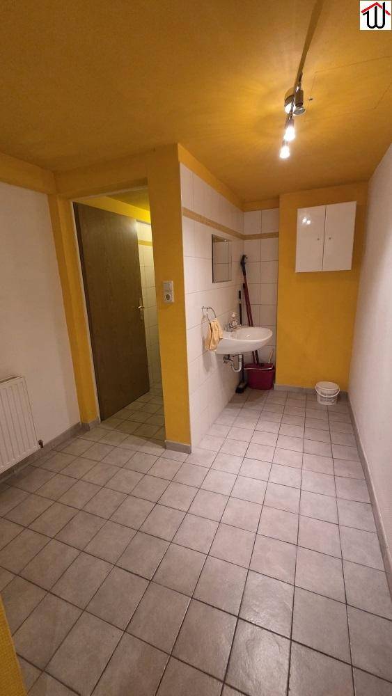 Funktionaler Raum mit Fliesenboden, Waschbecken und gelb gestrichenen Wänden.