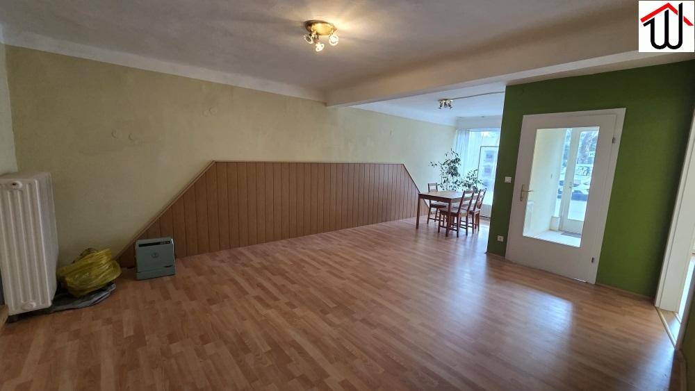 Geräumiger Mehrzweckraum mit Laminatboden, Heizkörper und einer Holztäfelung an der Wand.