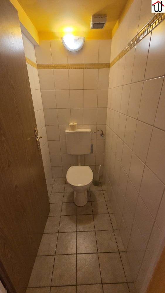Kleiner Toilettenraum mit hellen Fliesen, WC und einem Abluftventilator an der Decke.