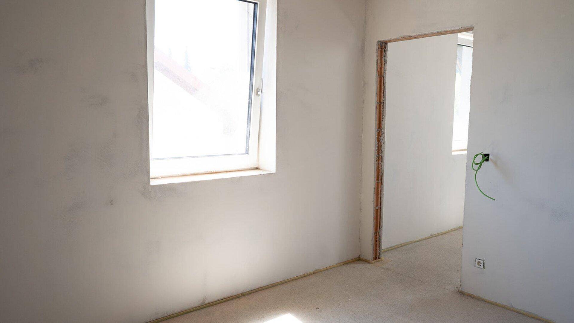 Heller, unfertiger Raum mit einem Fenster und offenem Türrahmen, bereit für den Innenausbau.