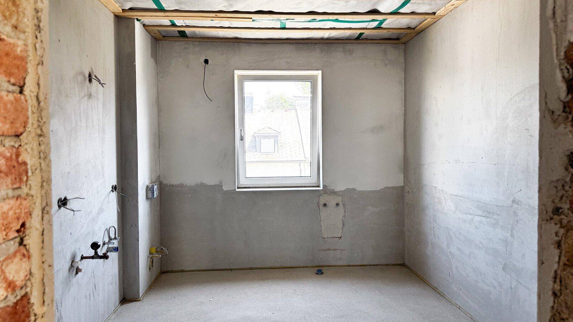 Unfertiges Badezimmer mit Fenster und vorbereiteten Anschlüssen, bereit für die Installation.