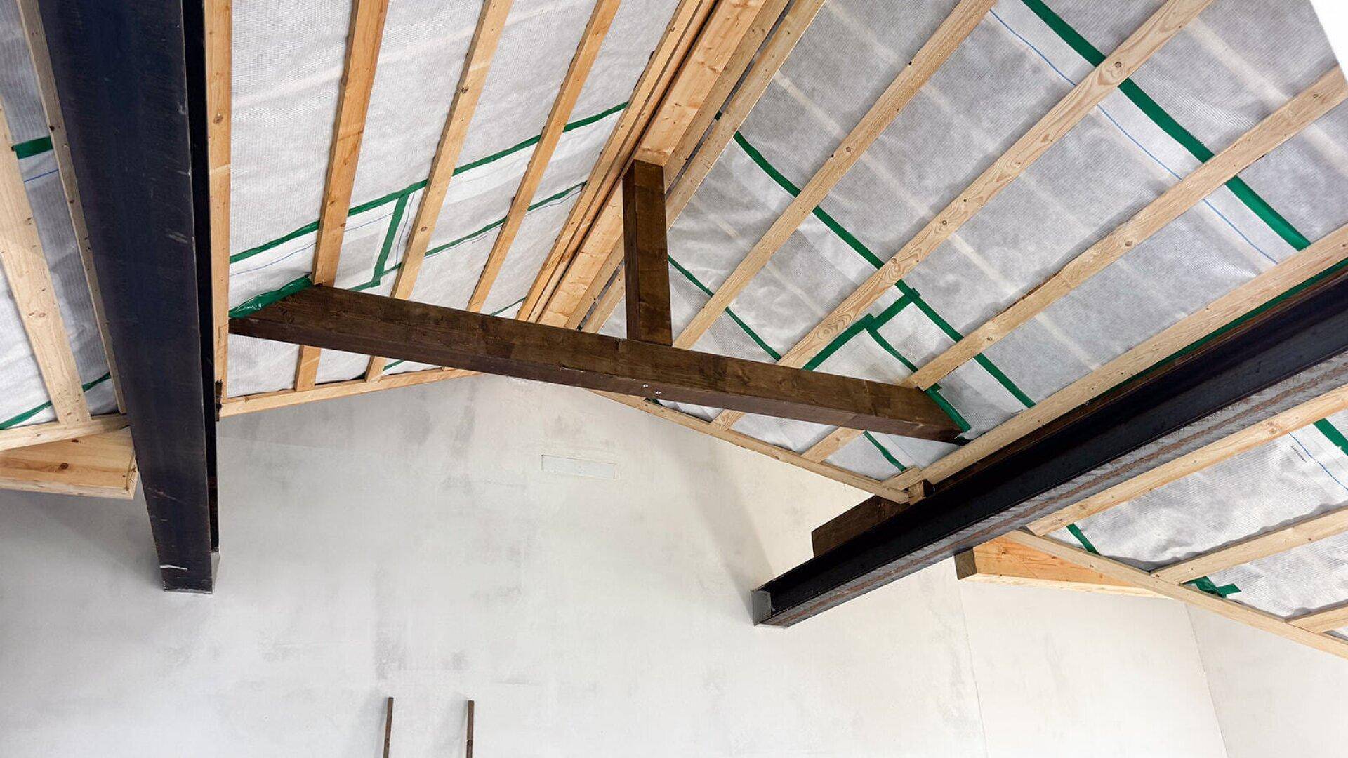 Detailansicht der Dachkonstruktion mit Holzbalken und Metallträgern, zeigt den Rohbauzustand.