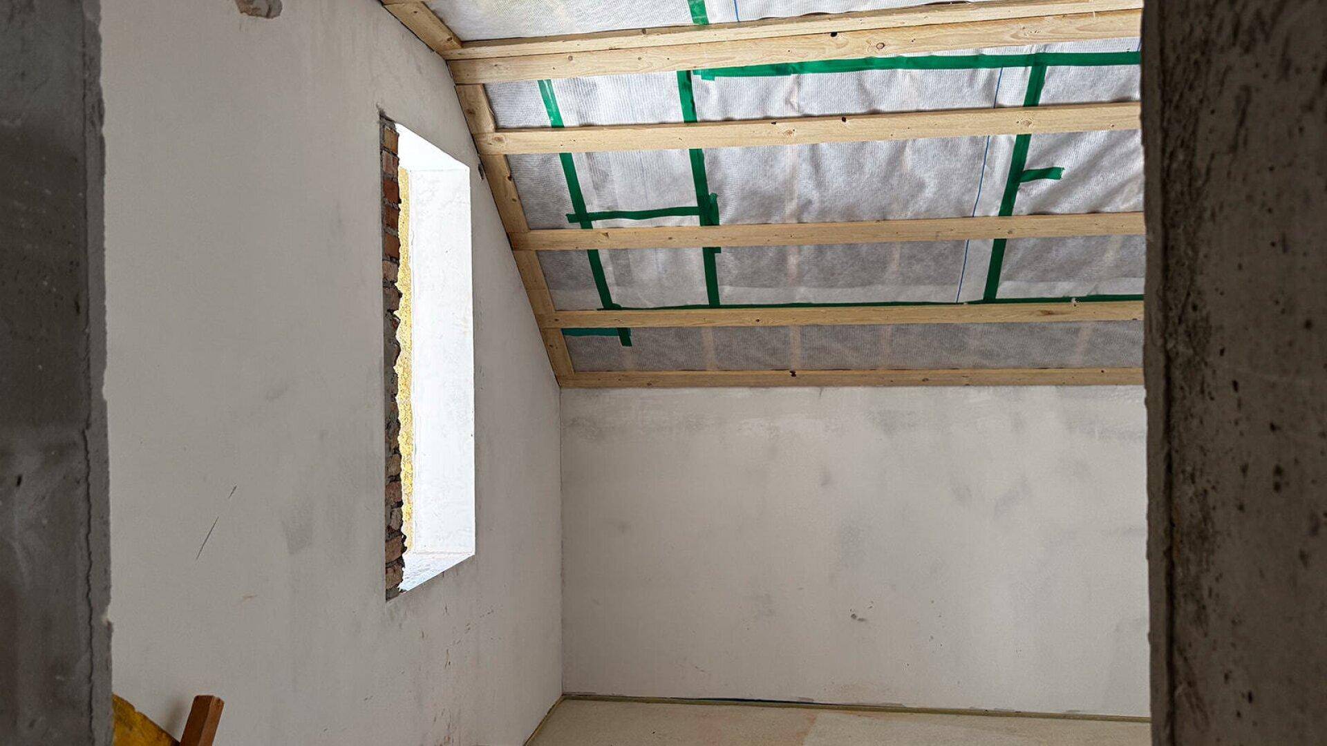Unfertiger Dachraum mit schrägen Wänden und sichtbarer Holzkonstruktion, wartet auf den Ausbau.