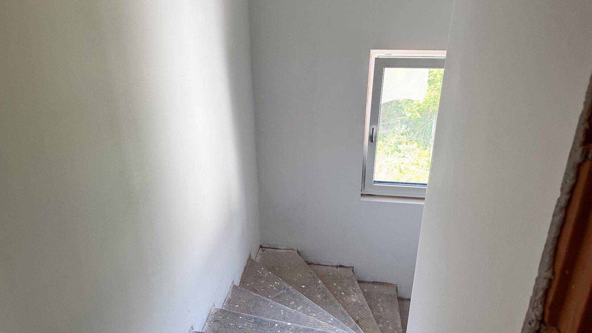 Unfertiges Treppenhaus mit Fenster, das natürliches Licht hereinlässt, bereit für den Endausbau.