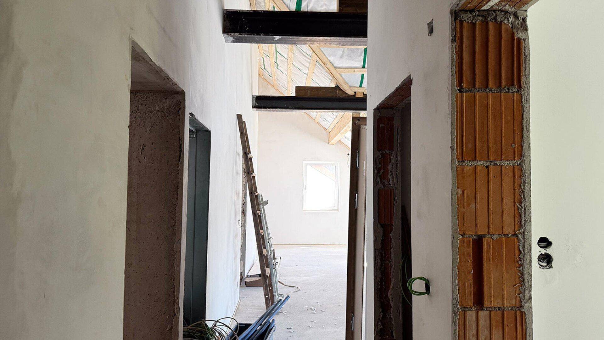 Blick durch einen Türrahmen in einen großen, unfertigen Raum mit sichtbarer Dachkonstruktion.