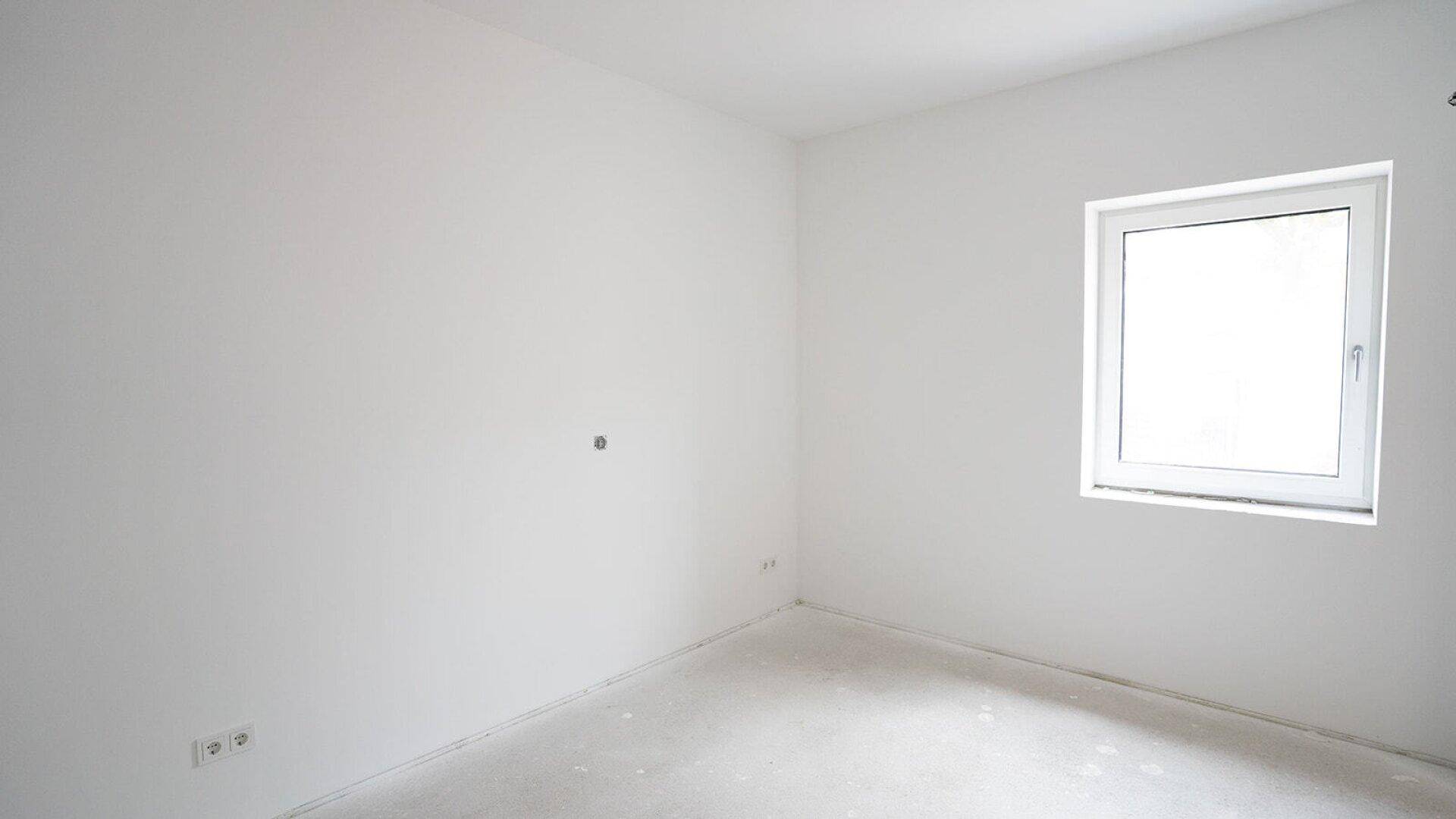 Unmöbliertes Schlafzimmer im Rohbau mit einem Fenster und weißen Wänden.