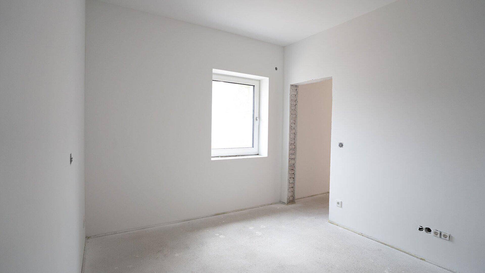 Leeres Zimmer im Rohbau mit einem Fenster und einem Türrahmen, bereit für den Ausbau.