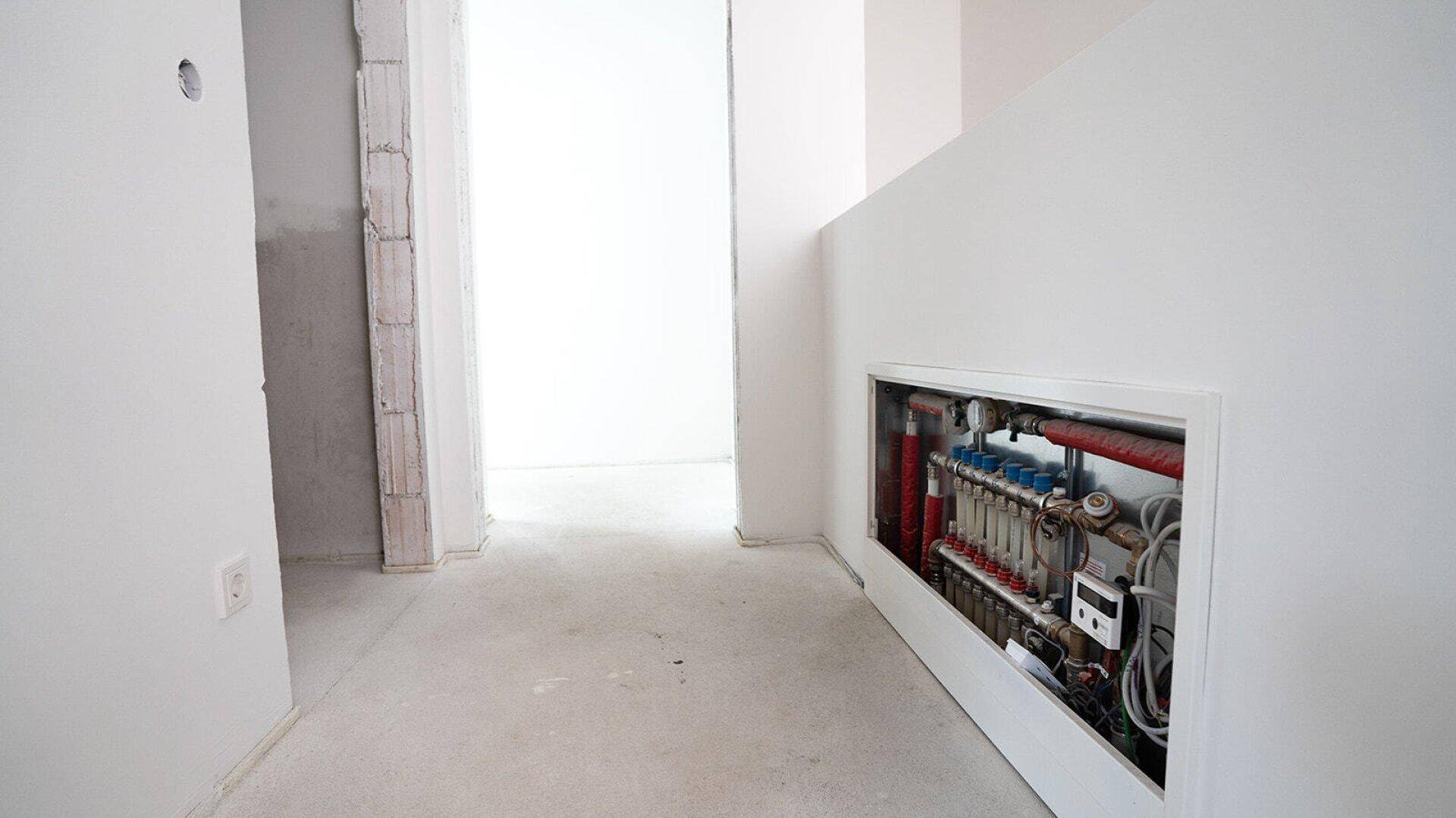Flur im Rohbau mit sichtbarer Fußbodenheizungsverteilung in der Wand.