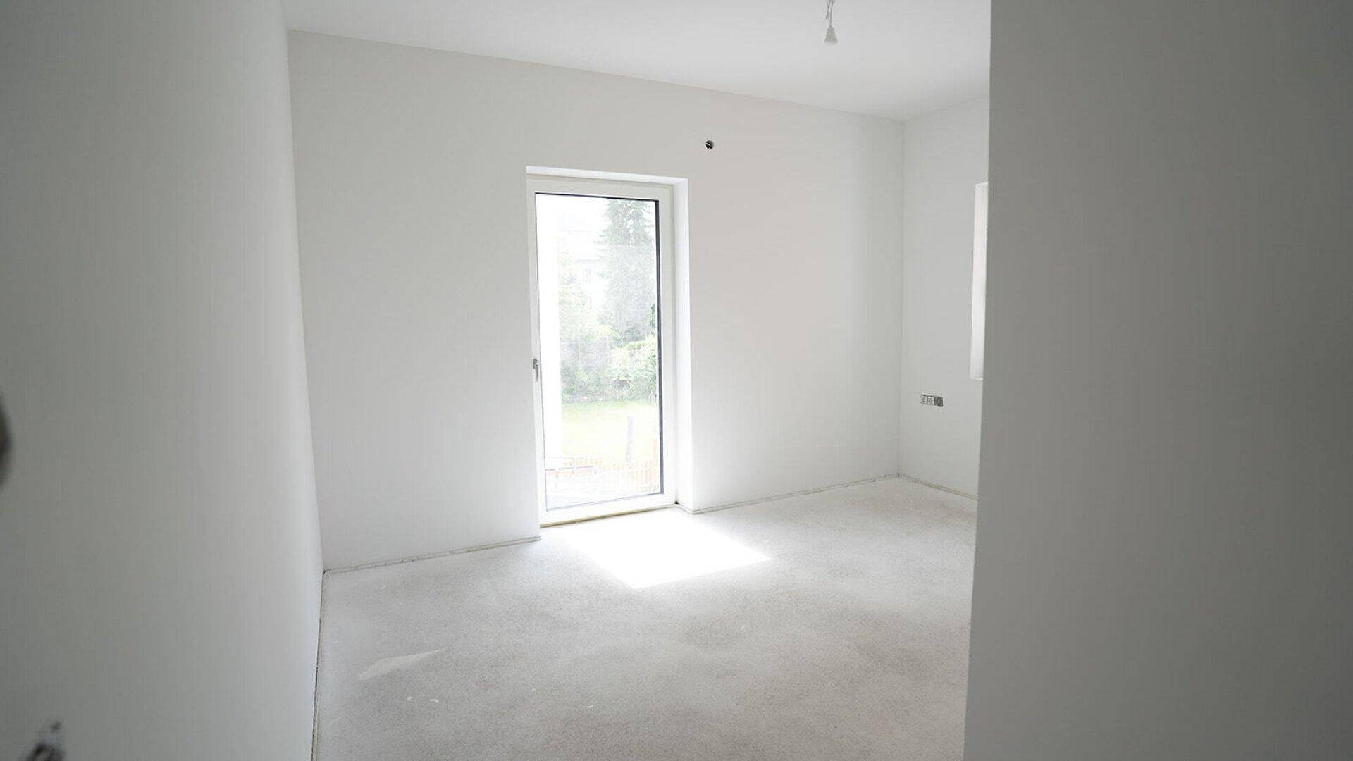 Helles Zimmer im Rohbau mit Zugang zu einem Außenbereich und viel Tageslicht.