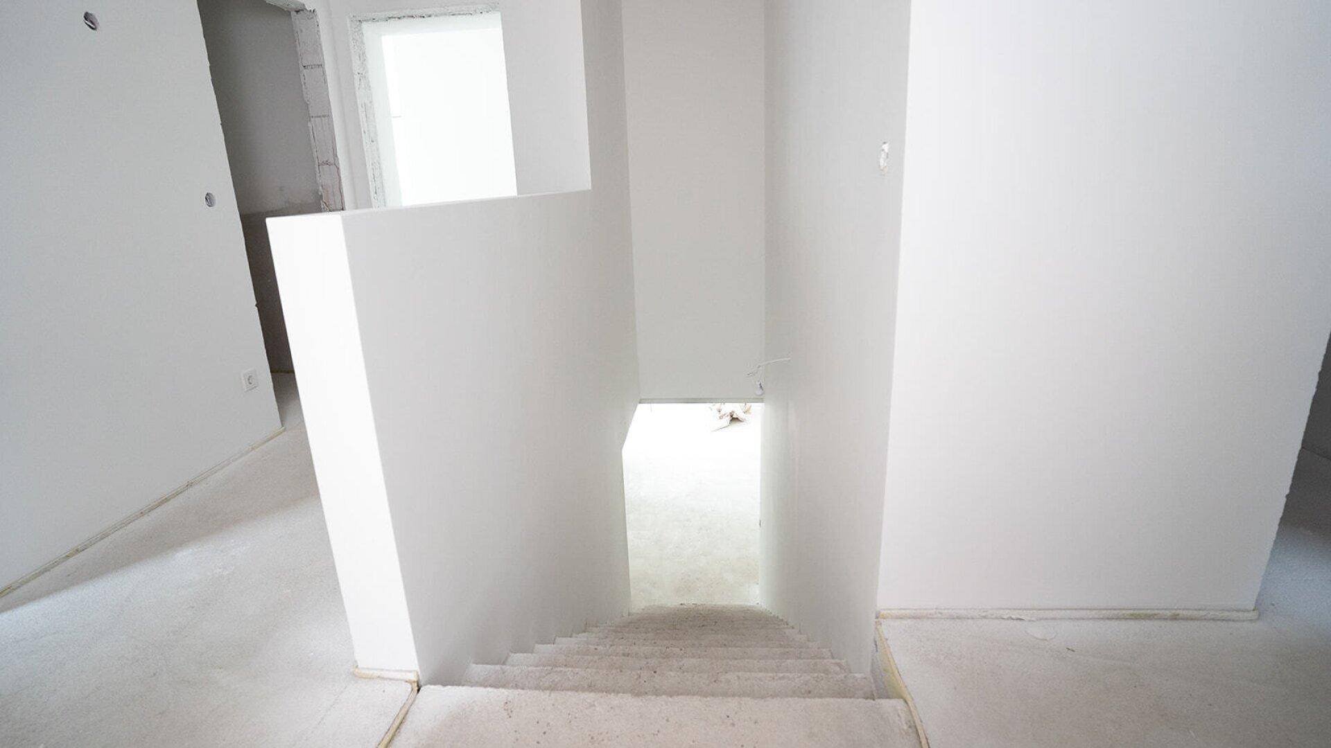 Treppenhaus im Rohbau mit weiß gestrichenen Wänden und Blick in das untere Geschoss.