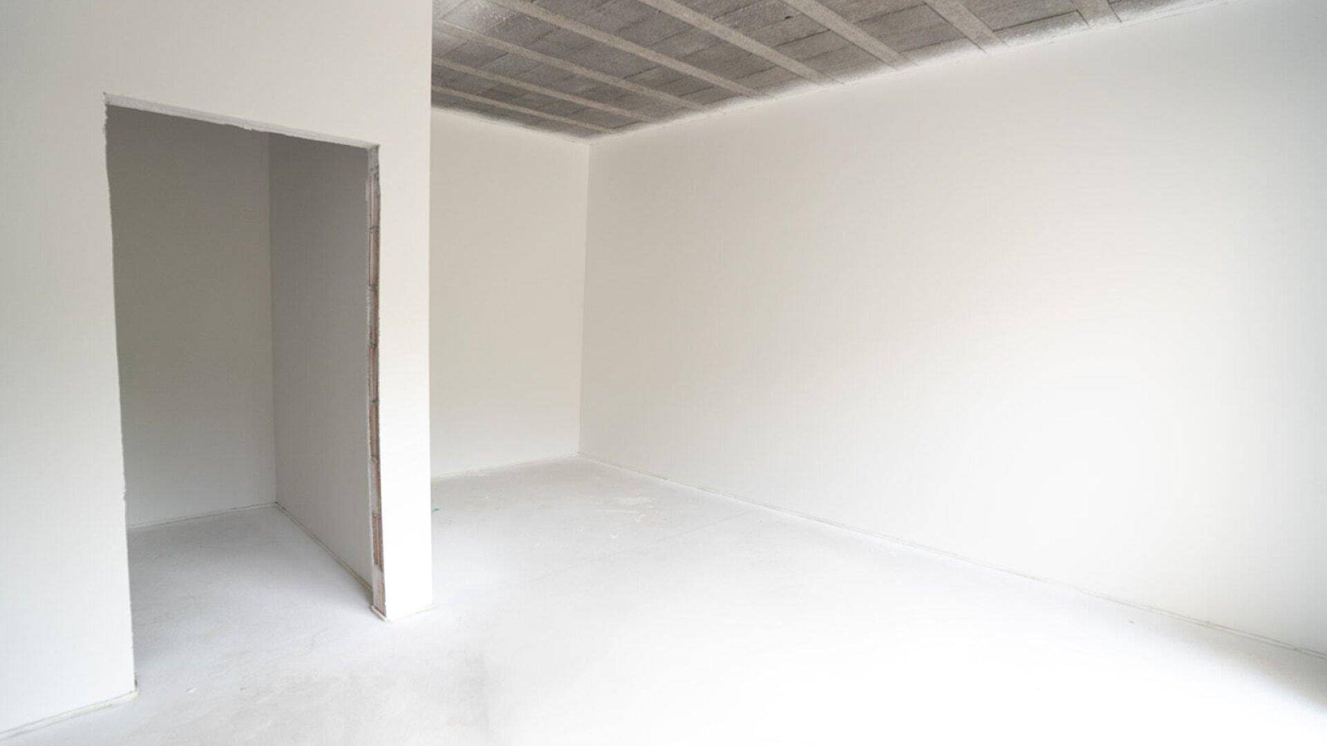Leeres Zimmer im Rohbau mit unfertiger Decke und weiß gestrichenen Wänden.
