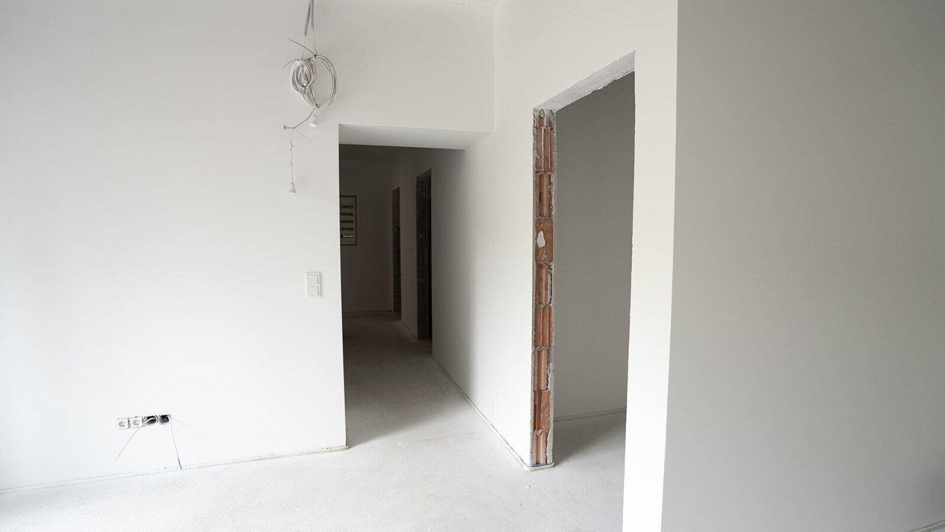 Flur im Rohbau mit mehreren Türöffnungen und sichtbaren Installationsbereichen.