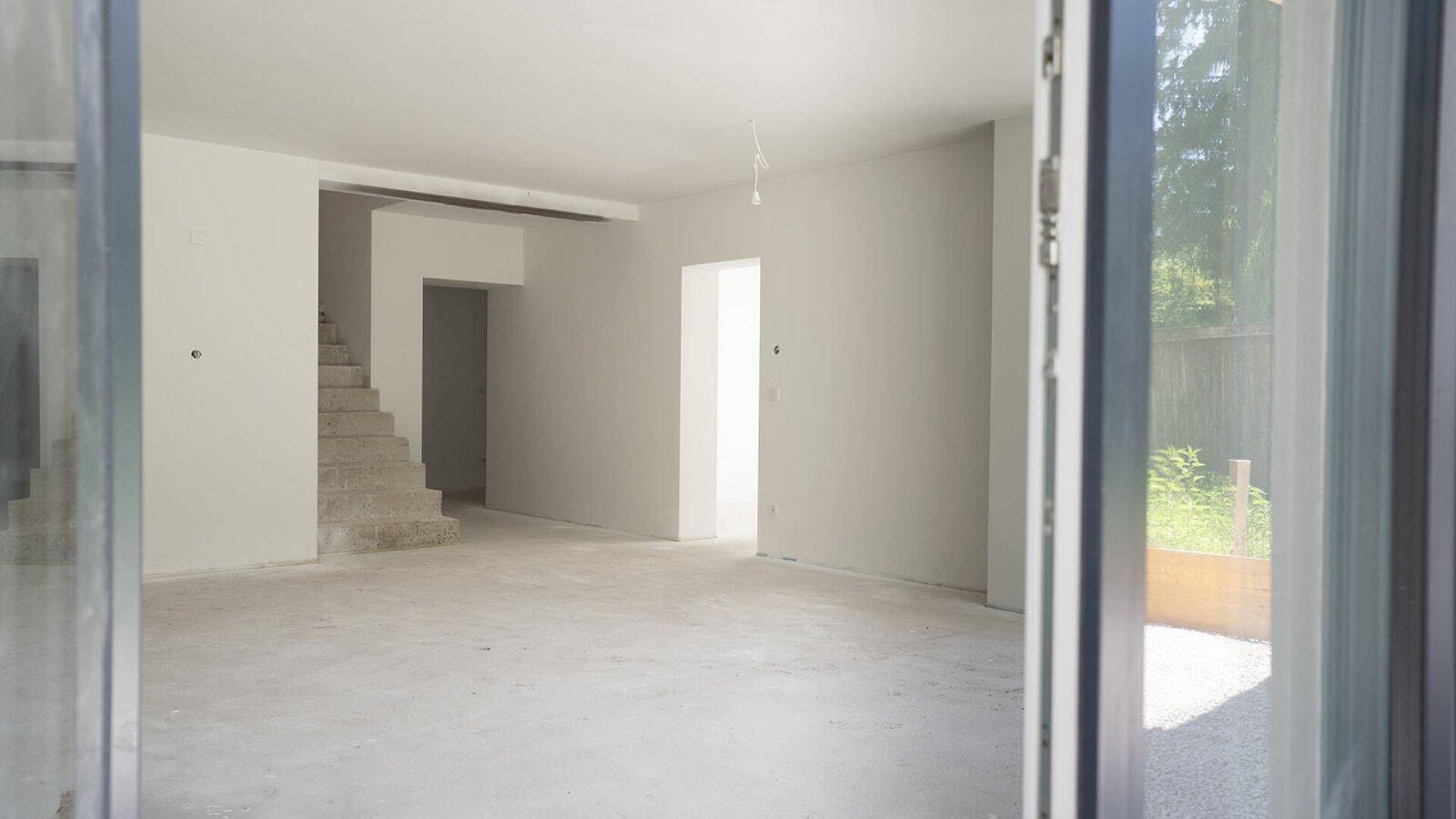 Geräumiger, unmöblierter Innenraum mit Treppenaufgang und viel Tageslicht.