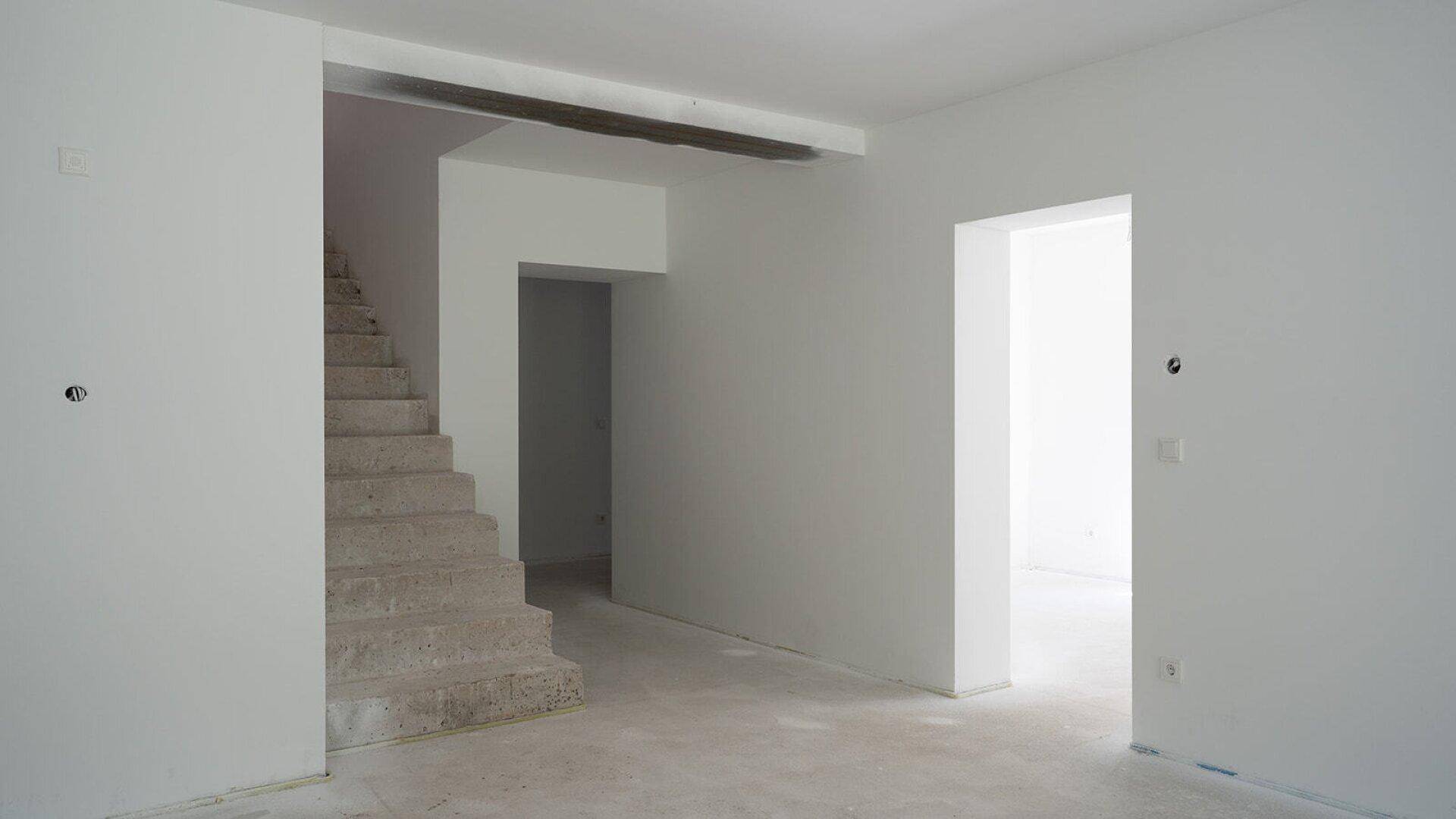 Geräumiger, unmöblierter Innenraum mit Treppenaufgang und viel Tageslicht.