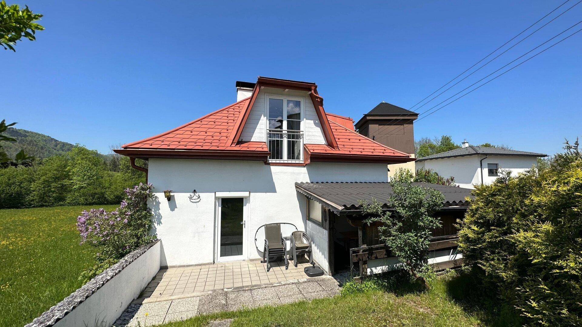 Rückseite des Hauses mit kleiner Terrasse, Rasenfläche und weitem Blick ins Grüne an einem sonnigen Tag.