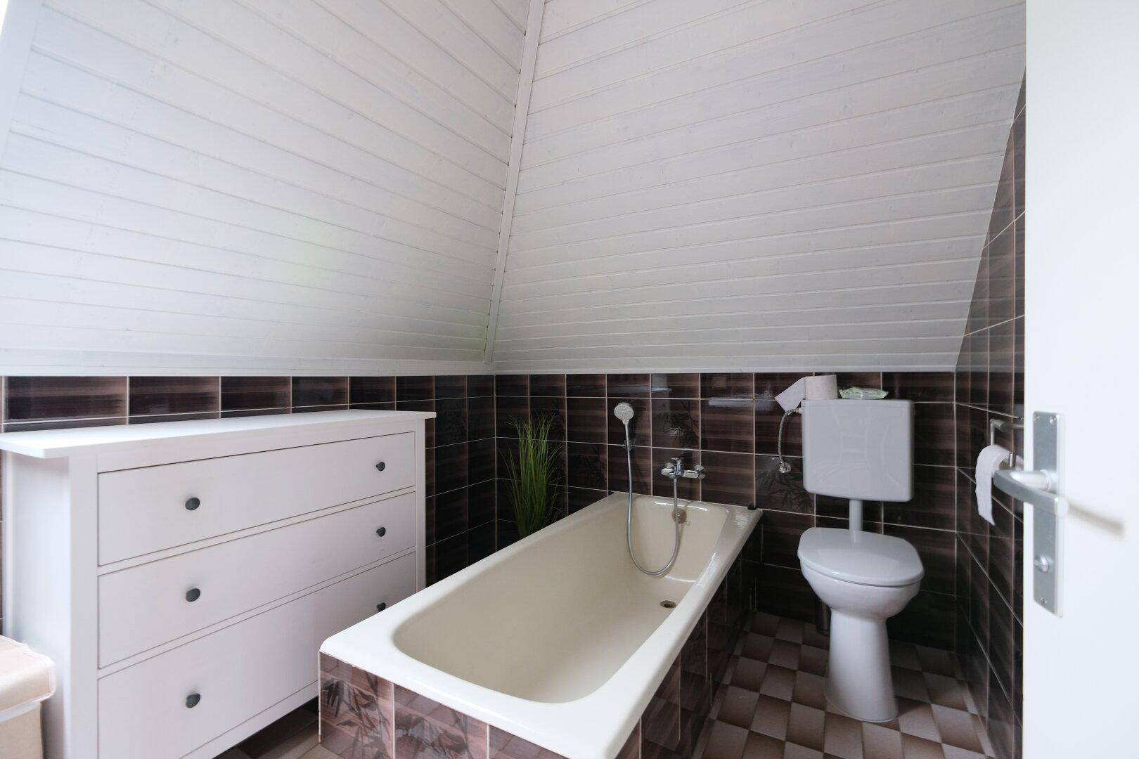 Dachgeschoss-Badezimmer mit Badewanne, Toilette und schrägen Wänden unter dem Dachfenster.