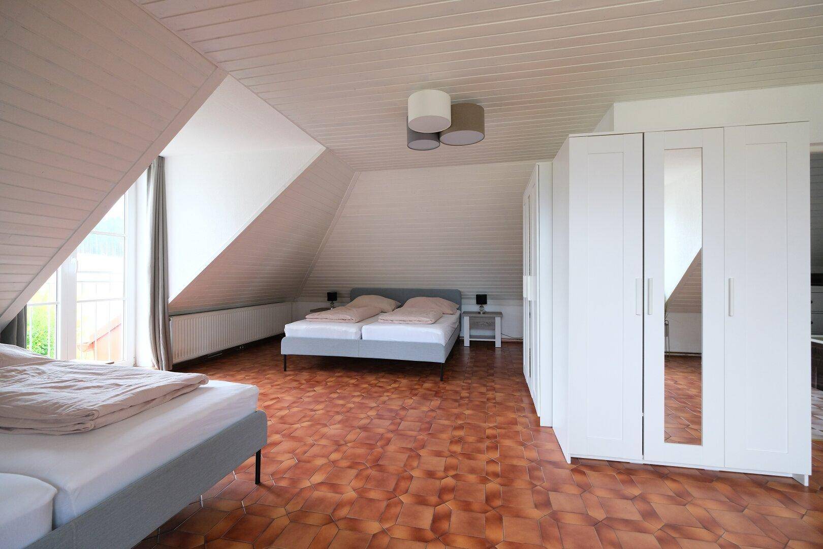 Schlafzimmer im Dachgeschoss mit Holzdecken, zwei Betten und weißen Kleiderschränken.