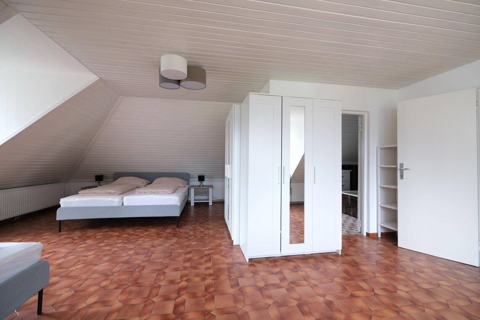 Helles Dachgeschoss-Schlafzimmer mit weißen Kleiderschränken und Zugang zu einem weiteren Raum.