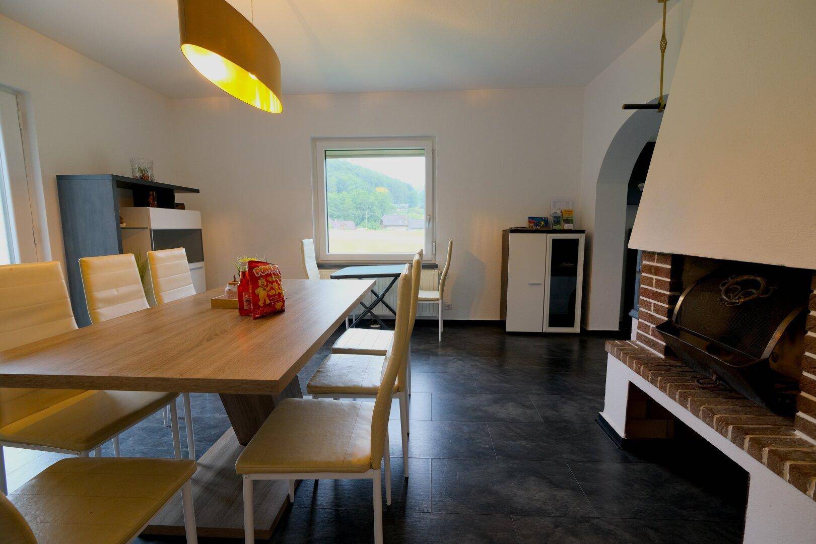 Heller Essbereich mit großem Holztisch, modernen Stühlen und einem Kamin, bietet Blick ins Grüne.