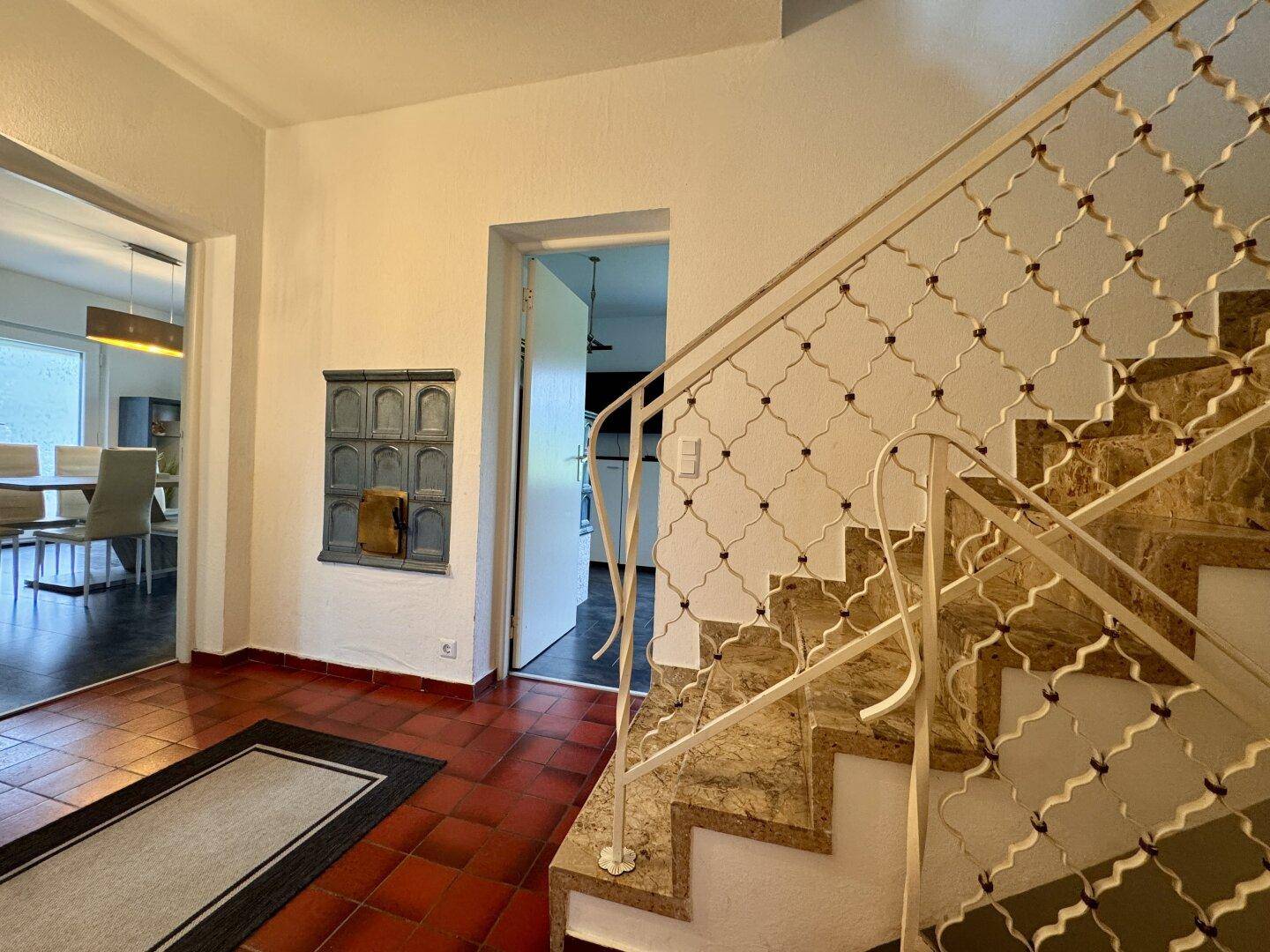 Geräumiger Flur mit Kachelofen, Marmortreppe und Zugang zu Esszimmer und weiteren Räumen.